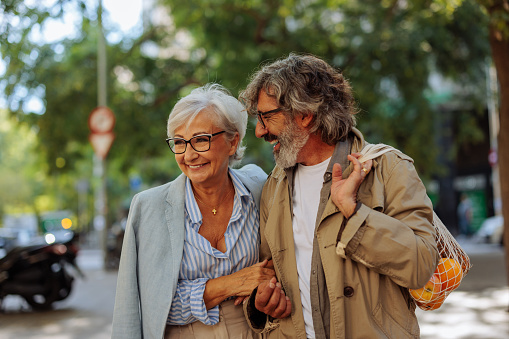 A happy senior couple are walking outside in the city and are laughing and having a good time together on a sunny day.