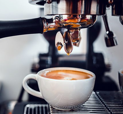 Extracción de café de la máquina de café con un portafiltro vertiendo café en una taza, poruing de espresso de la máquina de café en la cafetería photo