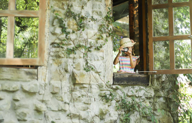 a smiling Asian girl take photos with a digital camera from a wooden window in a old house.