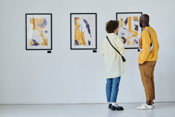 Young couple visiting art gallery Rear view of young couple visiting art gallery, they standing and watching modern art museum stock pictures, royalty-free photos & images