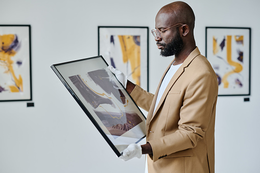 African guide examining modern art in his hands while working at art gallery