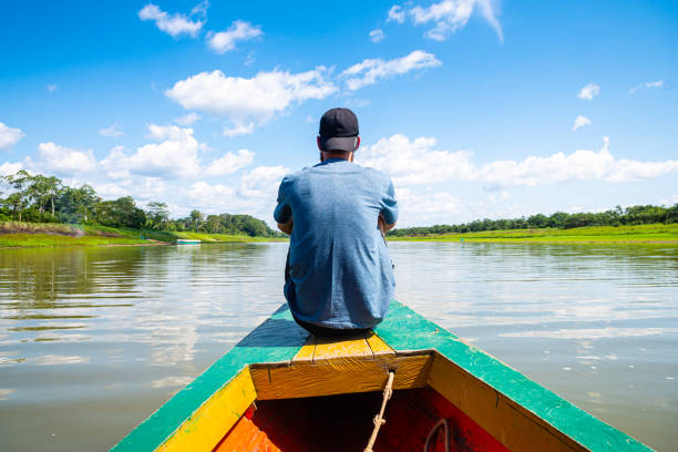 a man is sailing peruvian amazon on the front side of a wooden canoe a man is having a photo while is traveling in a wooden canoe throught amazon river in peru iquitos photos stock pictures, royalty-free photos & images