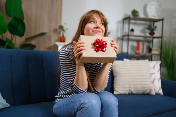 fille avec coffret cadeau assise sur un canapé à la maison - box white gift box flat photos et images de collection
