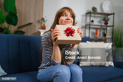 istock Girl with gift box sitting on sofa at home 1432877517