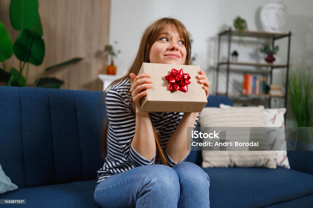 Girl with gift box sitting on sofa at home Gift Stock Photo