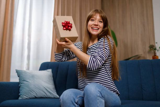 istock Happy young woman holding a gift box with present while sitting on sofa in appartment 1432877522