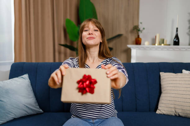 istock Joyful young woman who sitting on the sofa shows a gift package 1432877635