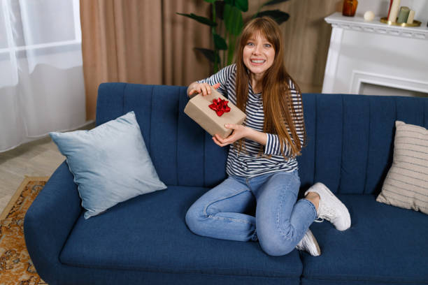 istock Surprised young woman with gift box sitting on sofa at home 1432877867