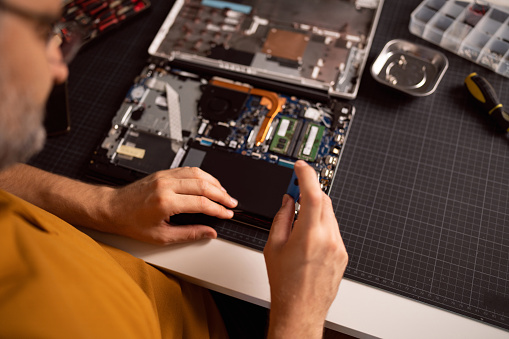 High angle view of unrecognizable Caucasian man with screwdriver disassembling laptop hard disk