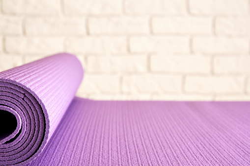 Purple thin yoga mat on the wooden floor in the modern gym. Workout and aerobic accessories