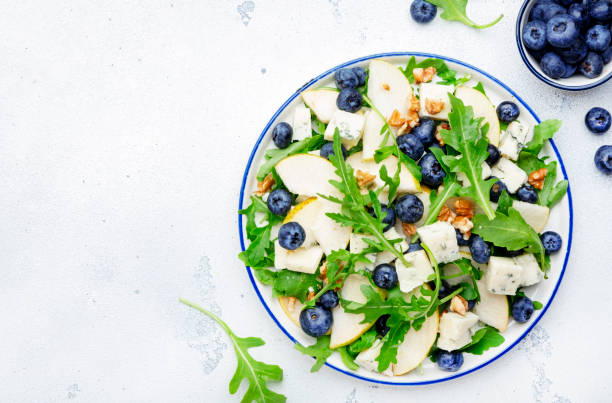 Delicious arugula salad with pears, blueberries, roquefort cheese and walnuts. Black kitchen table background, top view
