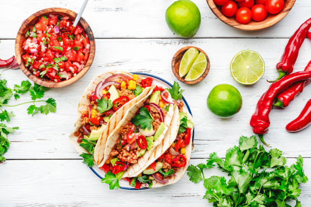 Mexican cuisine. Tacos with beef, corn, red beans, tomato salsa sauce and onions in corn tortilla on plate. White table background, top view stock photo
