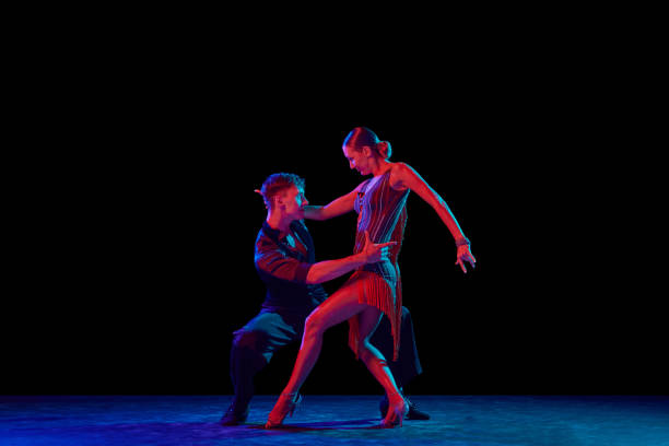 dos bailarines, bailarines de salón con trajes de elegancia en movimiento, acción sobre fondo oscuro en luz de neón. concepto de arte, música, danza, emociones. - tango fotografías e imágenes de stock