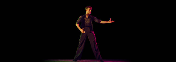 istock One young man, flexible male dancer in black costume standing alone isolated on dark background. Waiting for dance partner. Flyer for ad 1432885754