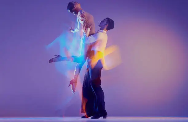 Photo of Young graceful dancers, flexible man and woman dancing ballroom dance isolated on gradient blue purple background in neon mixed light.