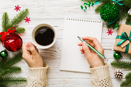 Woman writing Christmas to do list on notebook on colored background with xmas decorations.
