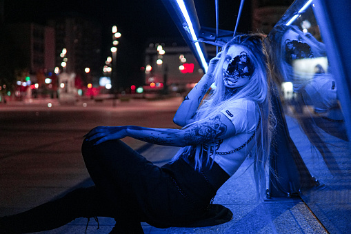 Halloween: Woman with sceleton face paint in the city, arm tattoo, portrait, fun in the city at night