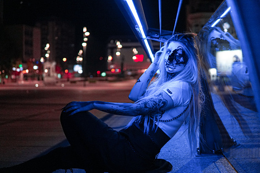 Halloween: Woman with sceleton face paint in the city, arm tattoo, portrait, fun in the city at night