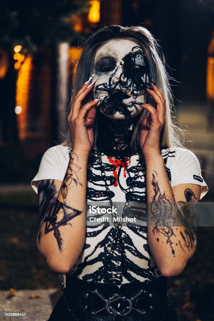 Woman with scary sceleton face painting mask and drawn tattoos on arms Halloween: Woman with sceleton face paint in the city, arm tattoo, portrait, fun in the city at night 25-29 Years Stock Photo