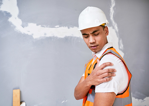 Construction worker holds shoulder in pain from workplace injury on site. High quality photo