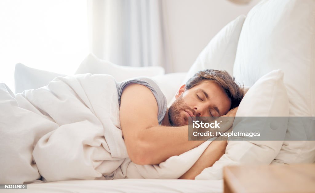 Home, bedroom and sleeping man in the morning lying his head on the pillow in apartment space. Tired, fatigue and relax male taking time off on the weekend in bed of airbnb or hotel accommodation Sleeping Stock Photo