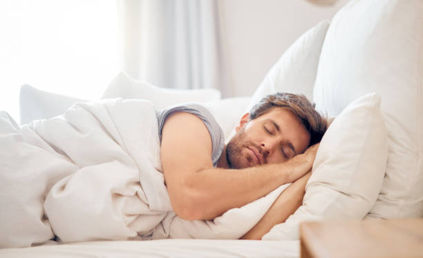 casa, quarto e homem dormindo de manhã deitado com a cabeça no travesseiro no espaço do apartamento. cansado, cansado e relaxe macho tirando folga no fim de semana na cama do airbnb ou acomodação de hotel - onírico - fotografias e filmes do acervo