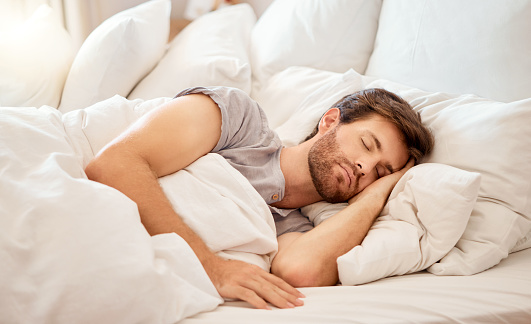 Relax, sleep and peace of a tired man sleeping in a bedroom bed at home. Dreaming, relaxing and resting calm attractive person with closed eyes on a pillow at his house in the morning taking a nap
