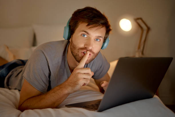 laptop, retrato e gesto silencioso da mão do homem tentando se concentrar. insônia ou leitura de e-mails workaholic à noite em seu quarto. expressão de silêncio da pessoa para ambiente silencioso enquanto trabalha. - silent night audio - fotografias e filmes do acervo