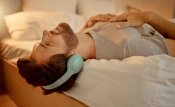 Happy man, streaming a podcast in bed smiling with headphones at home. Young guy listening to music from spotify on internet or radio to earphones, time to relax, life, peace in his apartment bedroom hombre feliz, transmitiendo un podcast en la cama sonriendo con auriculares en casa. chico joven escuchando música de spotify en internet o radio en auriculares, tiempo para relajarse, disfrutar de la paz en el dormitorio de su apartamento