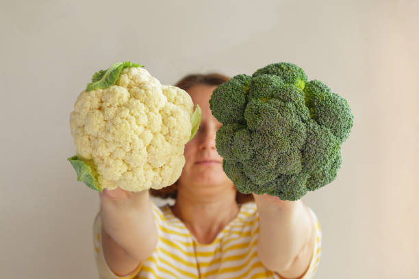 istock Woman covers her face with Fresh green broccoli and cauliflower. Selective focus 1432890349