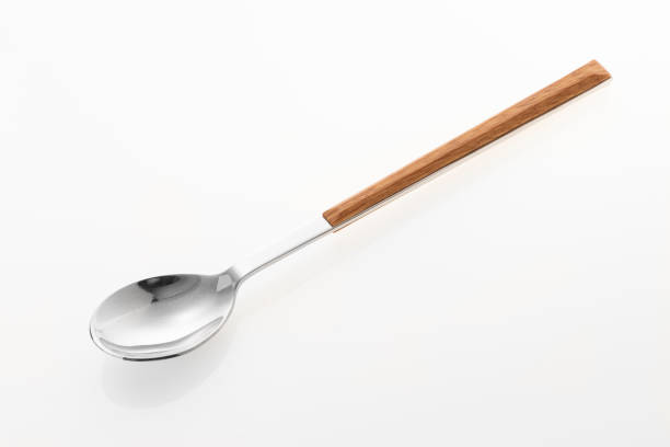 A dirty plate in a rustic style with a metal spoon and fork crossed on top, next to a leftover lemon slice garnish. The left side features a glossy brown wooden table background.
