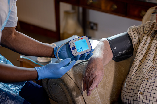 Close-up of an unrecognizable community nurse checking an unrecognizable senior man's blood pressure in his home. They are in the Northeast of England.