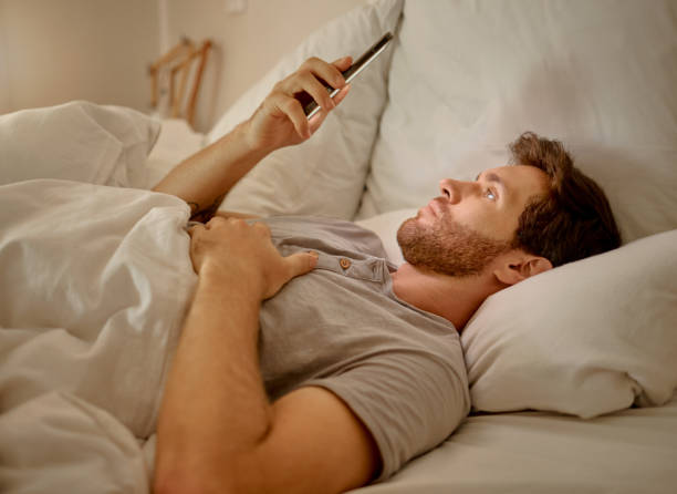 istock Social media, mobile app and relax man with smartphone using the internet or online website content at night in his bedroom with home wifi. Serious insomnia person reading blog for sleep health tips 1432892517