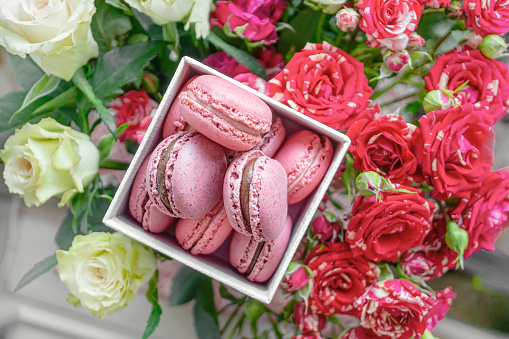 Delicate raspberry macaroons on the table with a bouquet of scarlet and white roses. Close up. Selective focus.