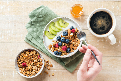 Granola yogurt bowl with fruits and berries for healthy breakfast. Woman eating granola with yogurt and fruits