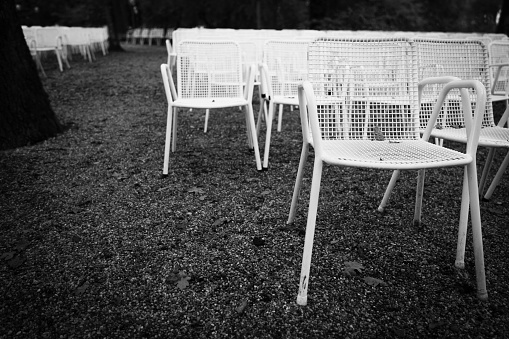Rows of white metal garden chairs in front of an outdoor stage. Series, 1of6