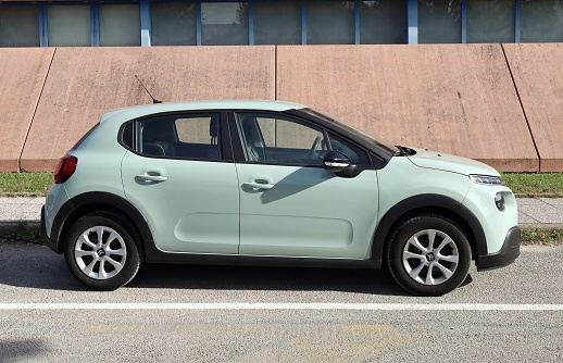 Udine, Italy. Otober 12, 2022. New light green Citroen C3 at the roadside with pink wall on background. Side view.