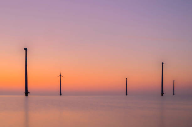 Wind turbines producing sustainable renewable energy in an offshore wind park in Flevoland, The Netherlands, during sunset. Long exposure photo creating an abstract view on the wind turbines with spinning blades.