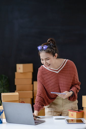 An Asian businesswoman works online shopping at her store. A young female seller prepares a parcel box to send to a concept customer. online selling ecommerce vertical image