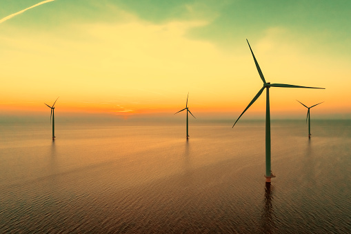 Wind turbines producing sustainable renewable energy in an offshore wind park in Flevoland, The Netherlands, during sunset. Drone point of view.