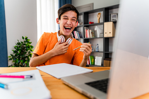 Teenage boy with headphones having online school class at home