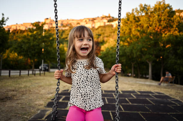 3 years old  girl having fun playing on the swing in an outdoor playground.