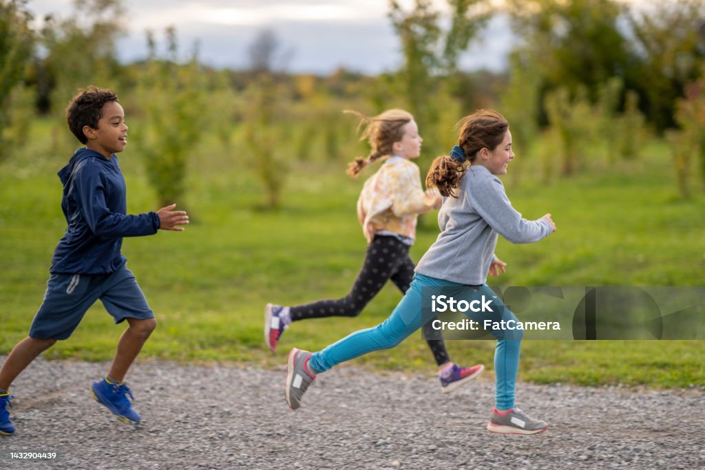 Children Running a Race A small group of children are seen running a Cross Country race in a small pack together. They are each wearing comfortable athletic wear and are focused on the path as they run towards the finish line. Child Stock Photo