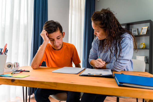 tutrice souriante aidant un jeune étudiant à faire ses devoirs. tutoriel et concept éducatif - adoption early teens teenager family photos et images de collection