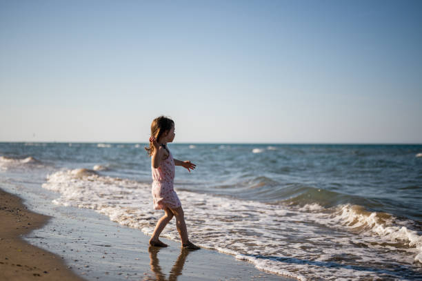 summer beach holidays lifestyle. kid Jumping in Ocean Waves at Beach. Girl having fun on beach. Happy little girl running and jumping in the waves. happy summertime holidays concept. feliz niña sonriente divirtiéndose corriendo en la orilla del mar al aire libre en la hora del atardecer. niños de estilo de vida feliz. estilo de vida de vacaciones de verano en la playa. niño saltando en las olas del océano en la playa.