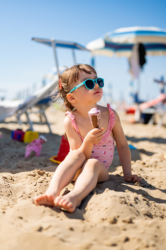Happy summer vacation on the beach. happy toddler girl wearing swimsuit and sunglasses eating tasty ice cream on a summer holiday day.