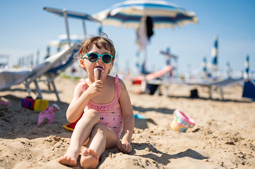Toddler girl eating ice cream on beach.eating ice cream outdoors. Happy girl at sea beach. Portrait of an adorable toddler eating ice cream on a beach.Happy little girl eating ice cream on beach.