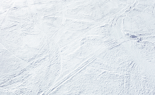An empty ski slope photographed from above, with ski tracks and curves from skiers turning on the snow.