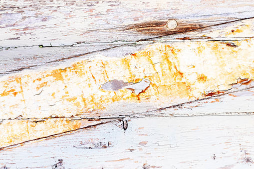 Close-up of an aged wooden surface, with signs of corrosion and other weathering, and with paint fading and peeling off.