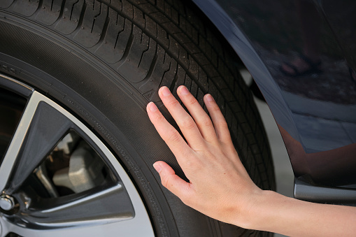 Female driver hands inspecting wheel tire of her new car. Vehicle safety concept.